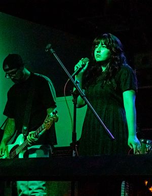 Musicians perform on stage bathed in green lighting with a guitarist and singer during a live concert.