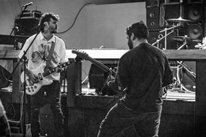 Two musicians perform on stage with guitars in a black and white concert photograph.