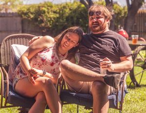 Two people sitting together and laughing in outdoor chairs on a sunny summer day in a backyard setting.