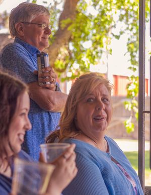 Three people enjoying beverages together at a gathering while standing in natural lighting by a window.