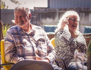 A senior couple sits outdoors in chairs and shares a joyful moment together on a sunny day.