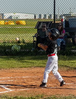 Youth baseball player in white uniform taking a batting stance at home plate during a little league game.