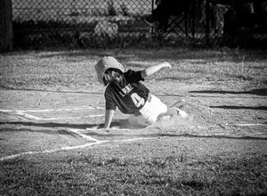 A baseball player slides into home plate during a game, creating a cloud of dust in this vintage black and white photograph.