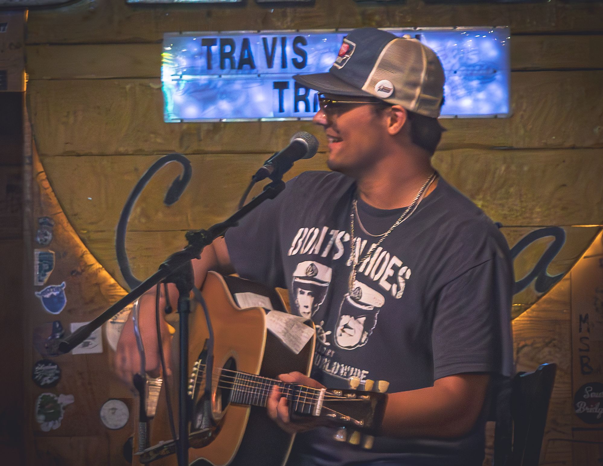 Country musician performs with an acoustic guitar under blue neon lighting at a small venue stage.