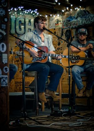Musician performing on acoustic guitar in dimly lit studio space with graffiti-covered walls.