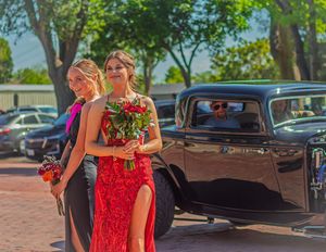 Formal couple in evening wear poses next to a vintage black car at a special event.