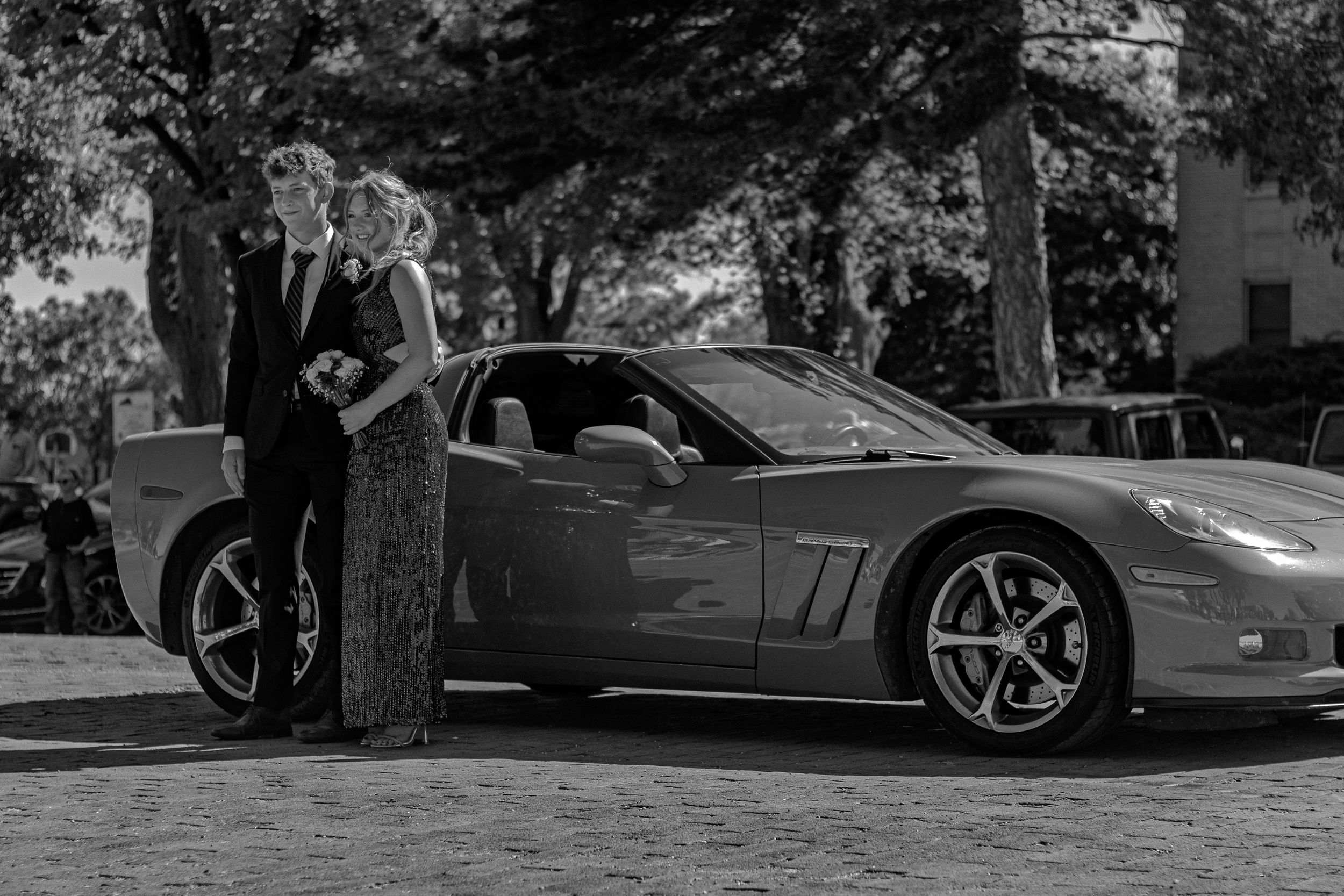 A sleek modern Corvette sports car parked under trees at a car show gathering.