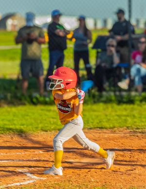 Youth baseball player in red helmet taking a swing at bat during a game on a sunny day at the diamond.