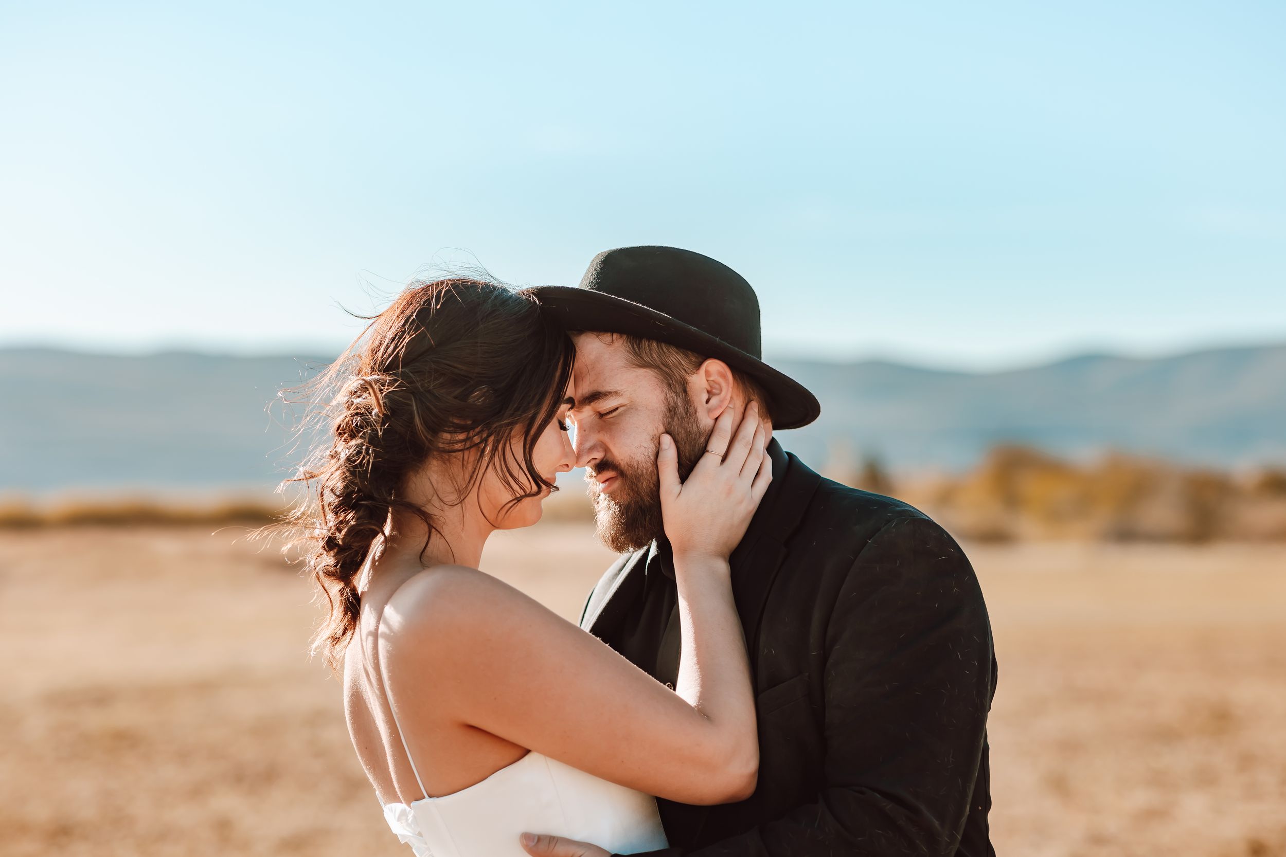 A romantic moment between a couple in black and white attire standing in a desert landscape at sunset.