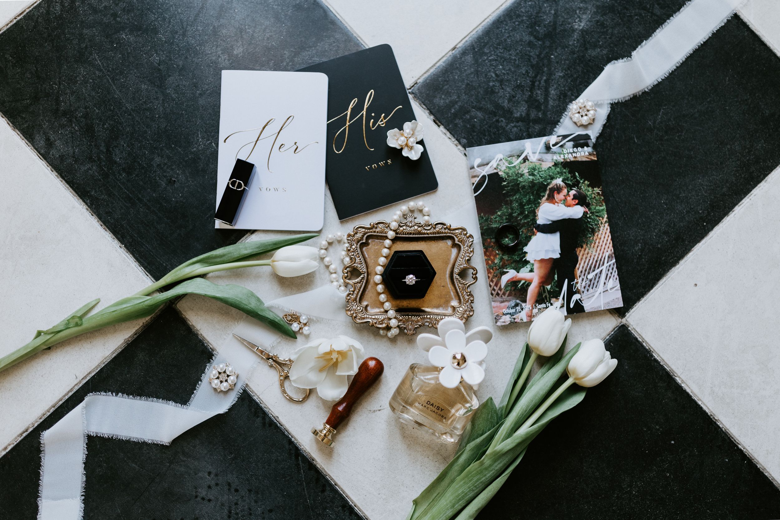 Wedding accessories including jewelry, fragrance, flowers and name cards arranged on a black and white geometric surface.