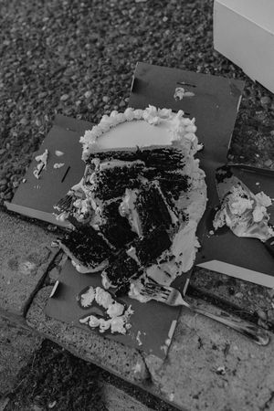 A smashed chocolate cake with white frosting lies broken and scattered on a dark surface with other baked goods around it.