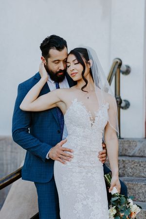 Newlyweds share an intimate moment on stairs as bride holds eucalyptus bouquet and wears lace wedding gown.