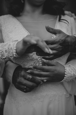Black and white close-up of hands touching while wearing white lace sleeves and delicate rings in an intimate moment.
