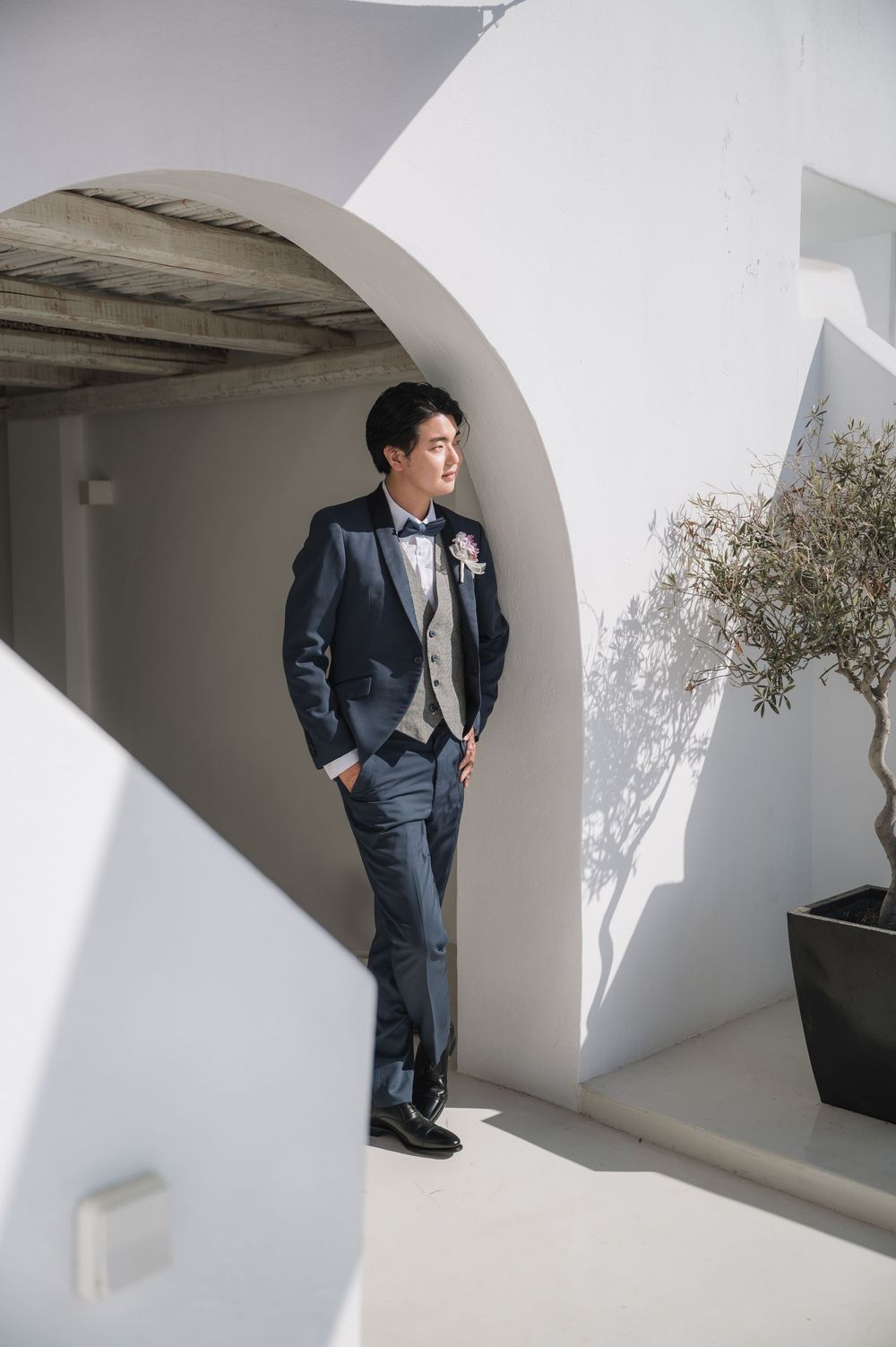 A stylishly dressed guest poses in a formal suit beneath a white arched doorway at a luxury venue.