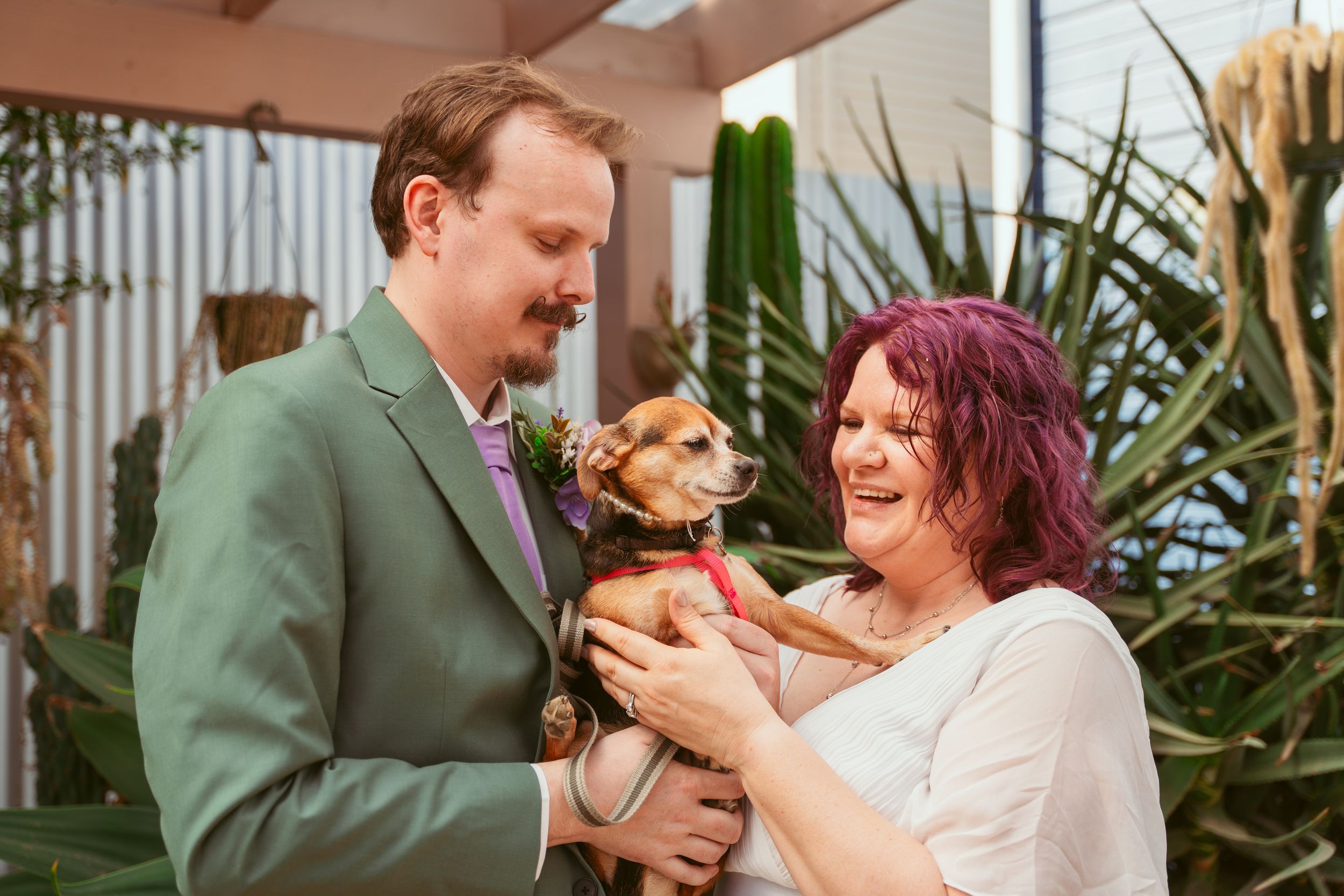 A couple shares a happy moment during their wedding celebration while holding a small dog in their arms.
