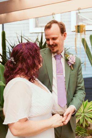Two people share an intimate moment during a wedding ceremony in front of lush greenery and a blue wall.