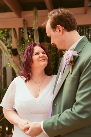 Happy couple shares an intimate moment during their wedding ceremony, with bride in white dress and groom in mint green suit.