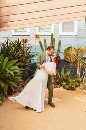 A romantic dip pose in front of a succulent garden with white wall and desert plants in the background.