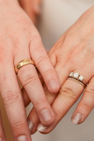 Close-up shot of two hands displaying wedding rings, one with a gold band and one with diamonds.