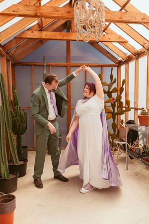Couples shares a joyful dance moment together in a greenhouse filled with cacti and wooden beams overhead.