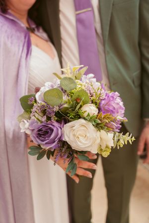 A stunning wedding bouquet featuring purple and white roses with mixed greenery against formal attire.