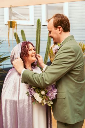 A tender moment between newlyweds in front of cacti, with the bride in pink and groom in sage green.