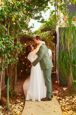 A couple shares an intimate moment under string lights and greenery in a garden wedding setting.