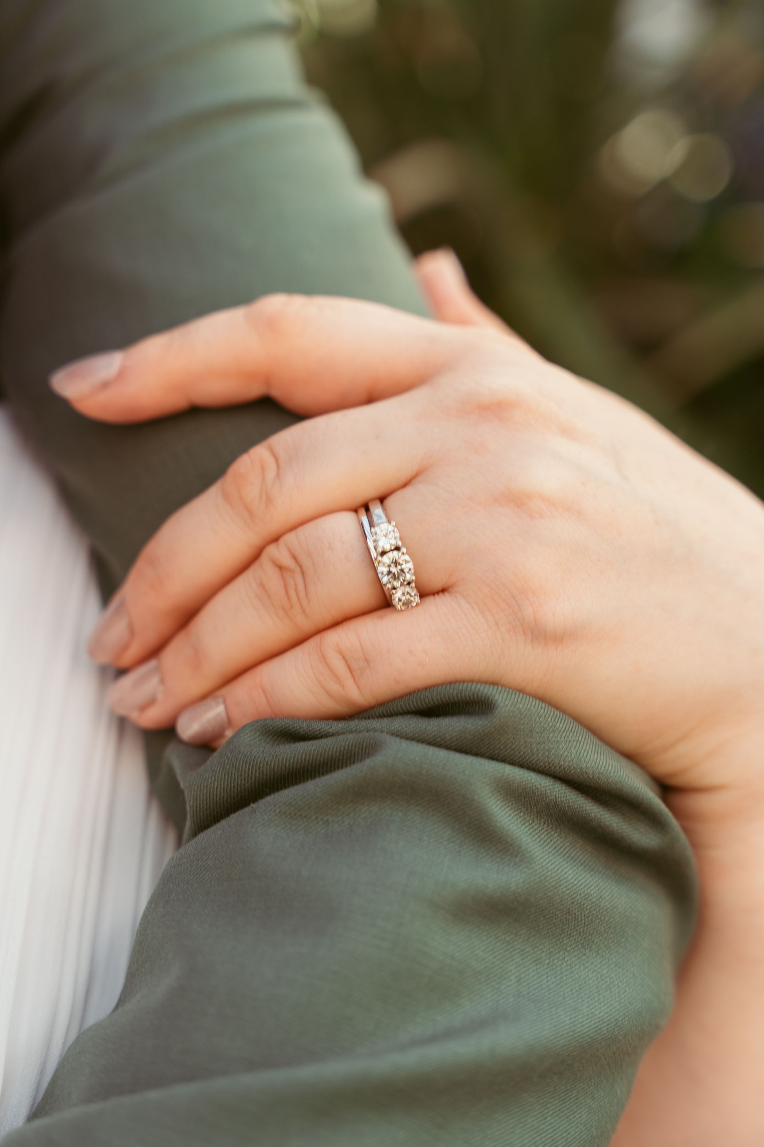 Close-up of wedding rings and hands against sage green and white fabric backgrounds.