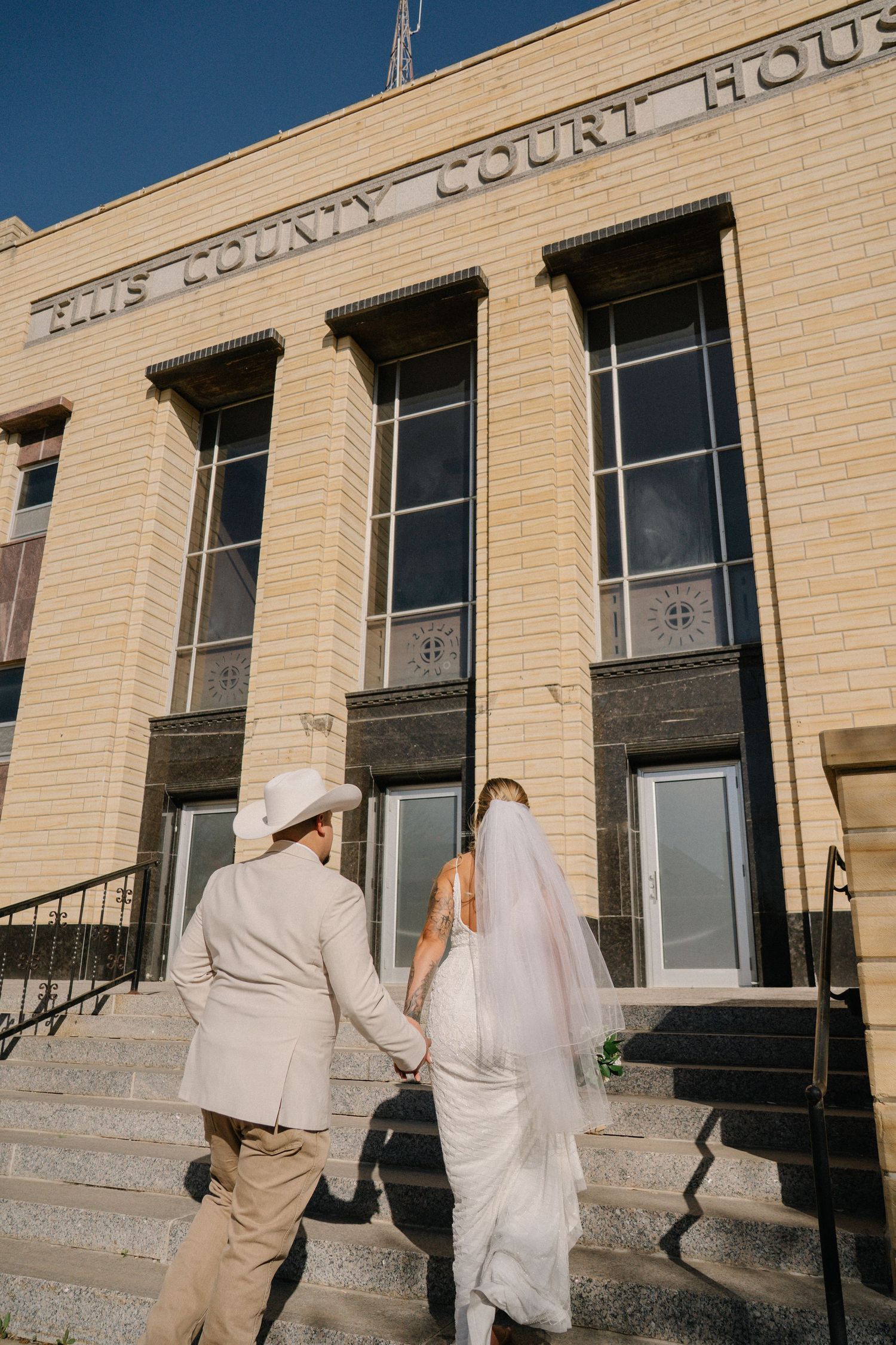 A couple embraces during their wedding ceremony in a courthouse with an American flag and large wall mural visible.