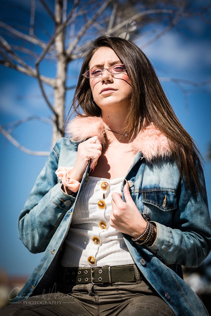 Winter fashion shot featuring a denim jacket with pink fur collar against bare tree branches.