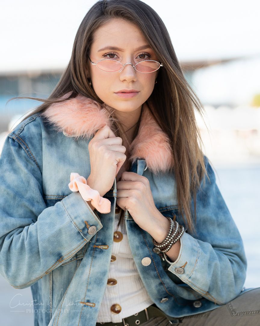 Close-up fashion portrait showing stylish eyewear and a denim jacket with pink fur collar.