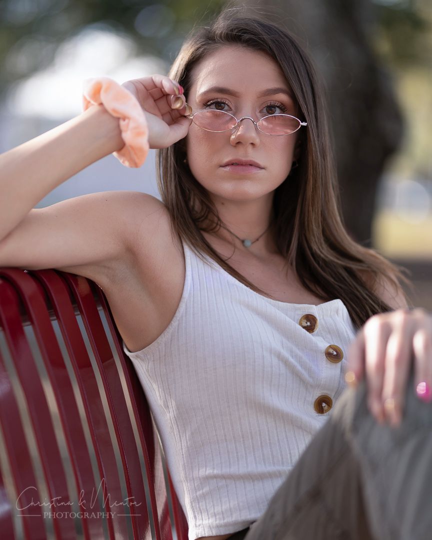 Summer fashion portrait on red bench wearing white button-up tank top and glasses.