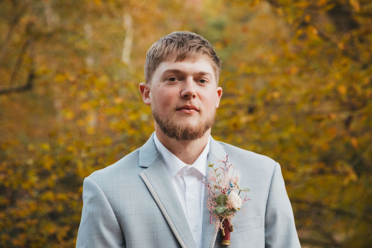 Autumn wedding portraits of groom in light gray suit with boutonniere.