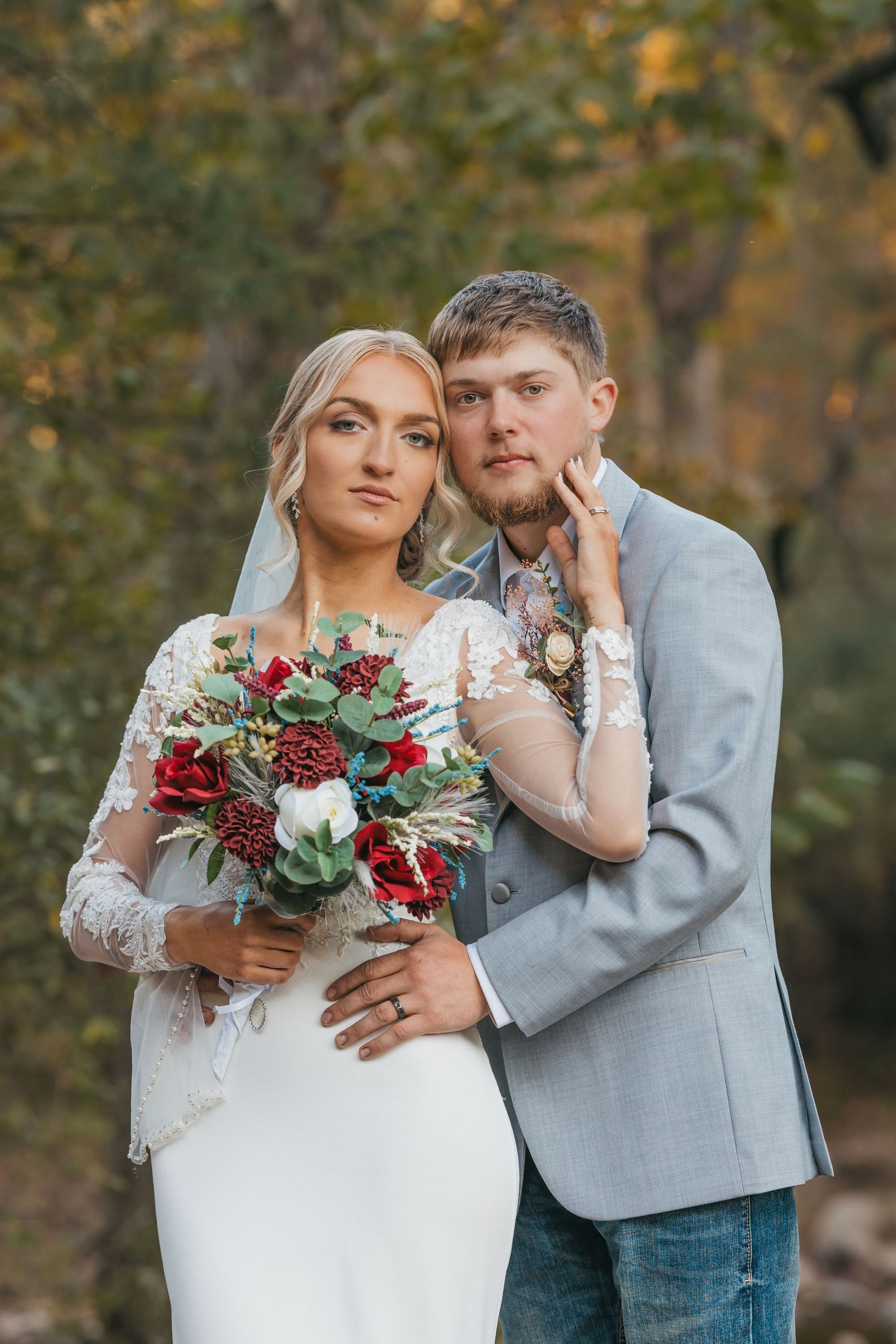 A couple shares an intimate moment in their wedding attire with a beautiful burgundy and greenery bouquet in an autumn setting.