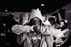 Black and white photo of person in hoodie with Greek symbols posing indoors.