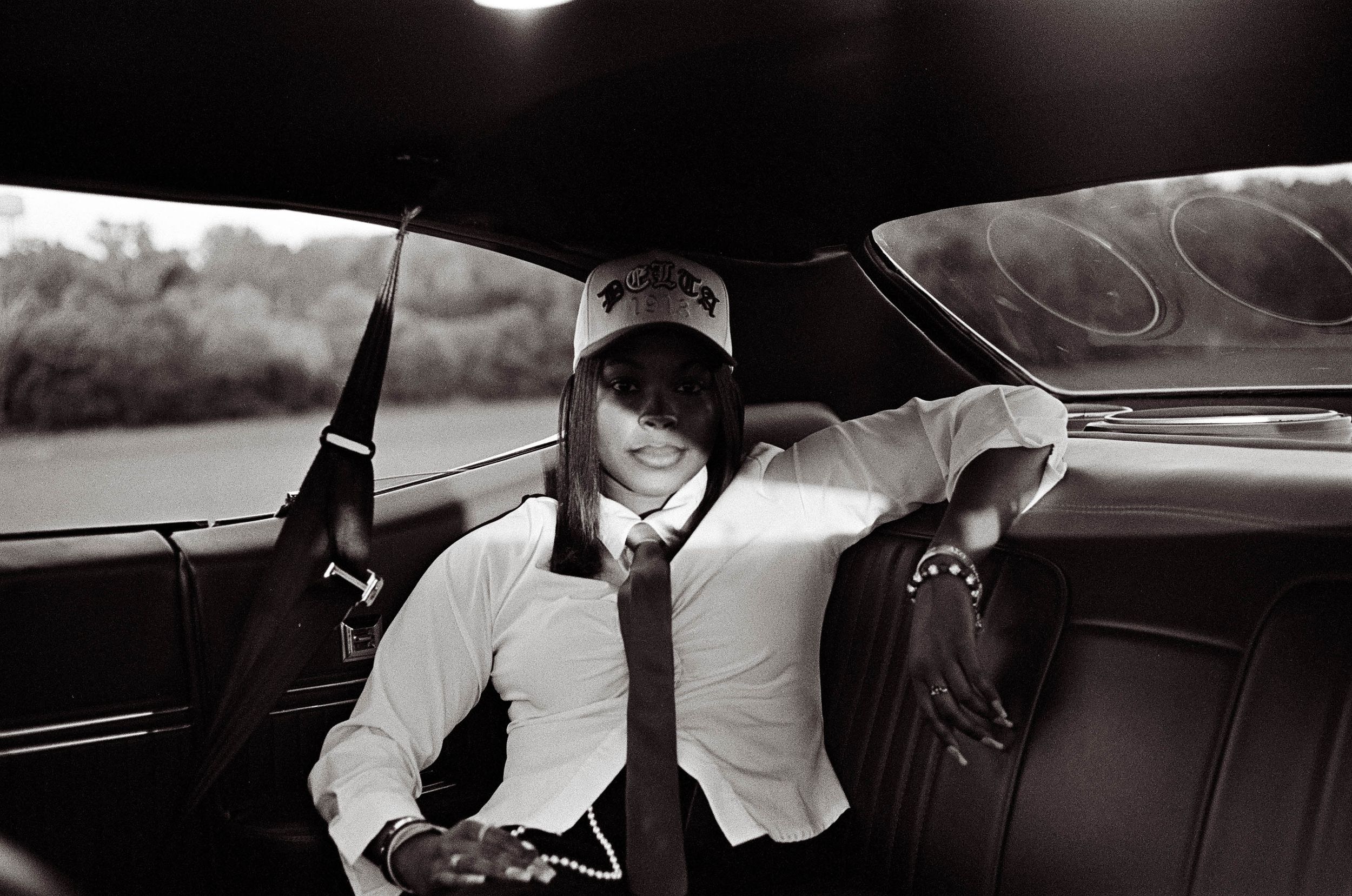 Black and white photo of person in cap sitting in vintage car interior.