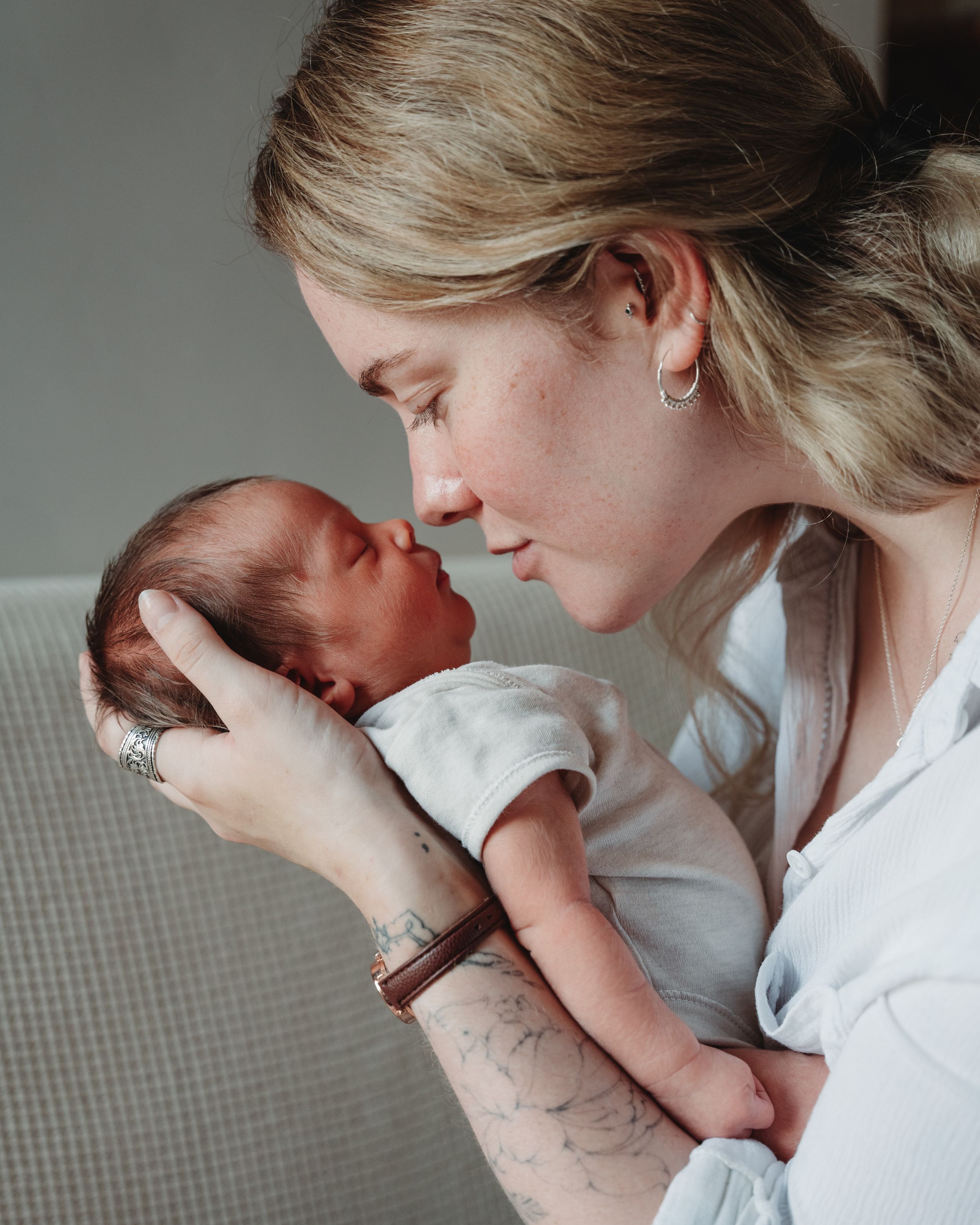A tender moment showing a mother in white cradling and gently nuzzling her newborn baby against a neutral background.