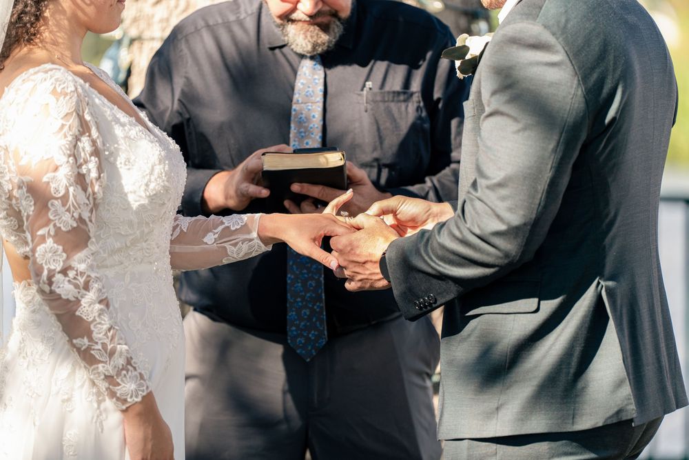 Bride and groom exchanging rings during wedding ceremony with officiant holding Bible.
