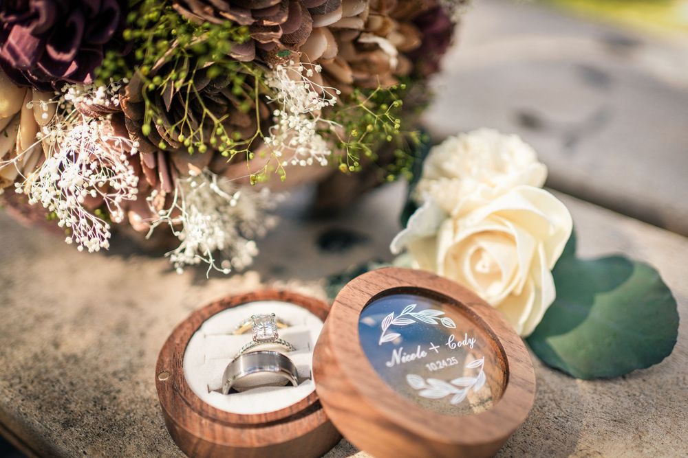 Elegant wedding rings displayed in a wooden ring box beside a bridal bouquet and white roses.