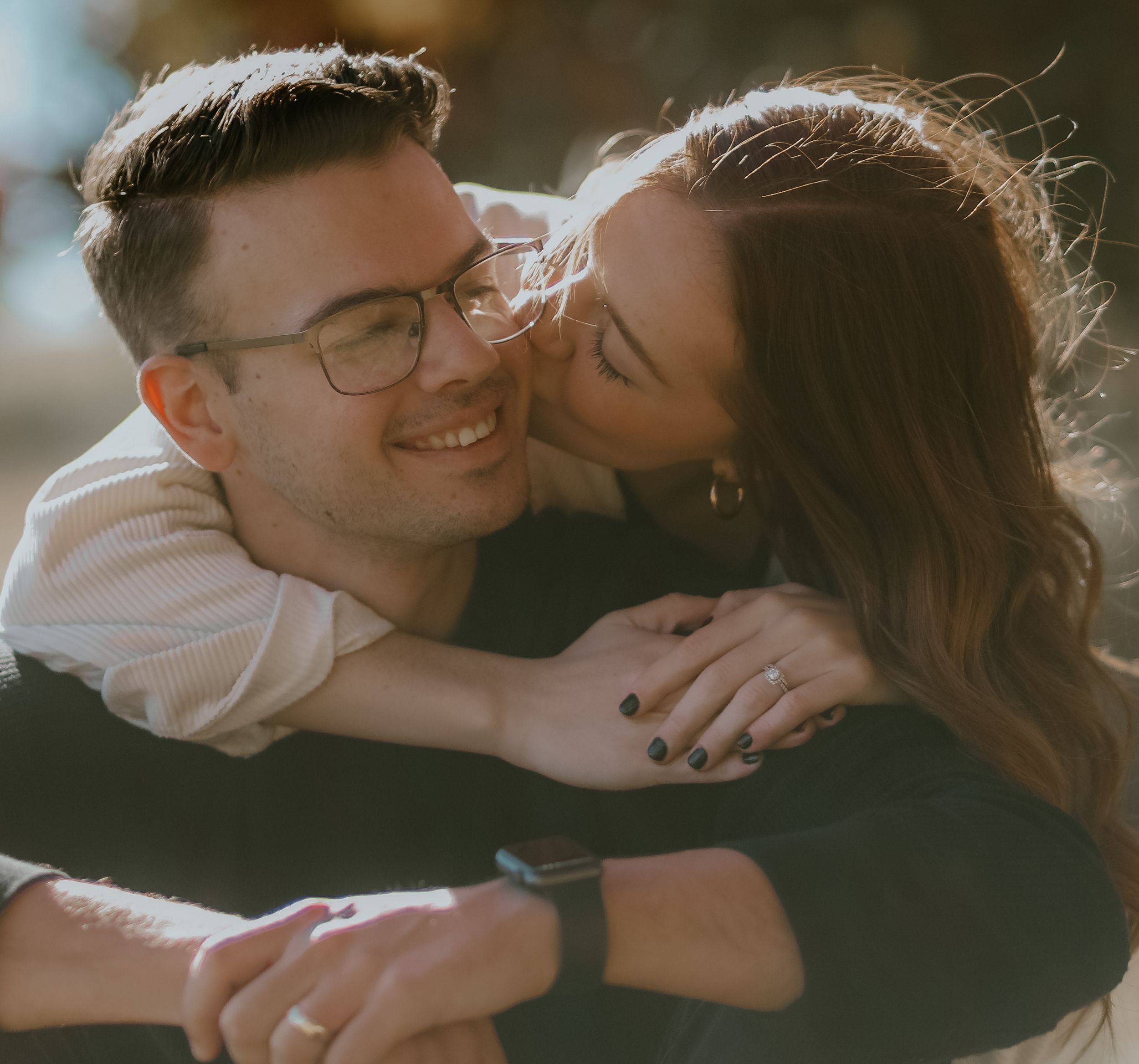 Two people in warm clothing embrace intimately in a monochrome outdoor setting with mountains in the background.