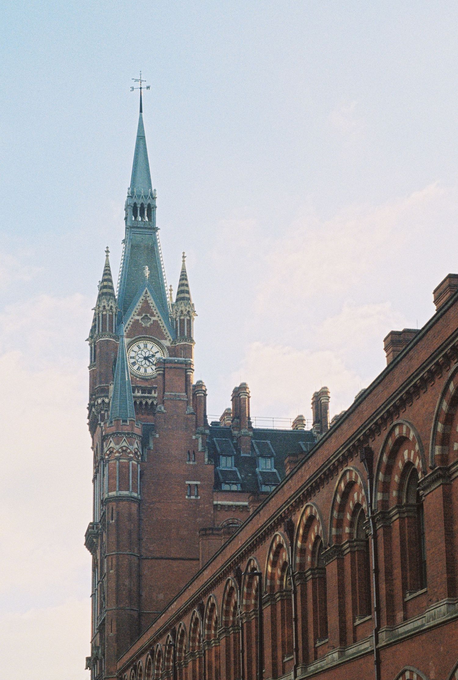 Gothic clock tower with spires rises against pastel sky at St Pancras station in London.