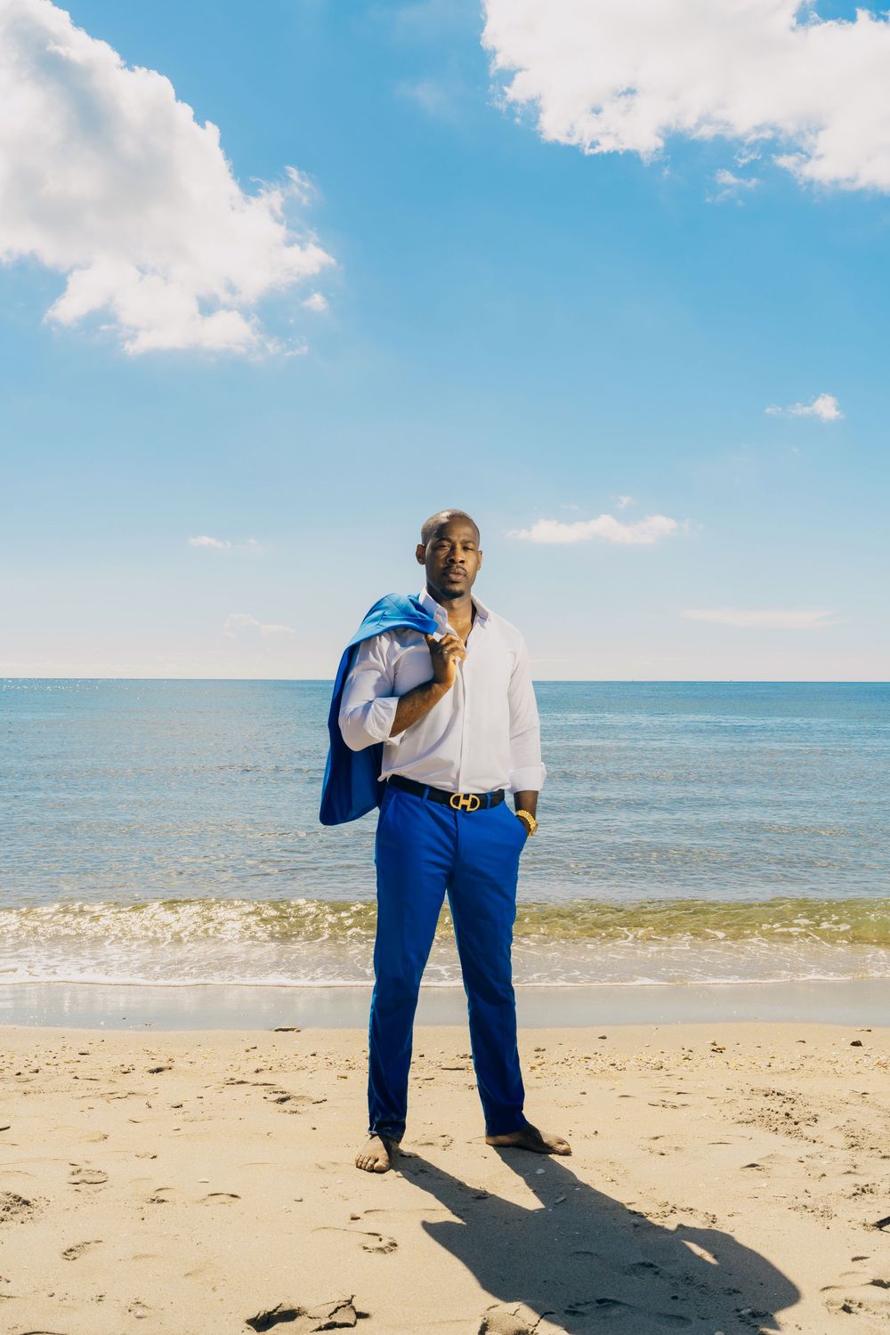 A figure in crisp business attire stands on a sunny beach with bright blue waters and sky in the background.