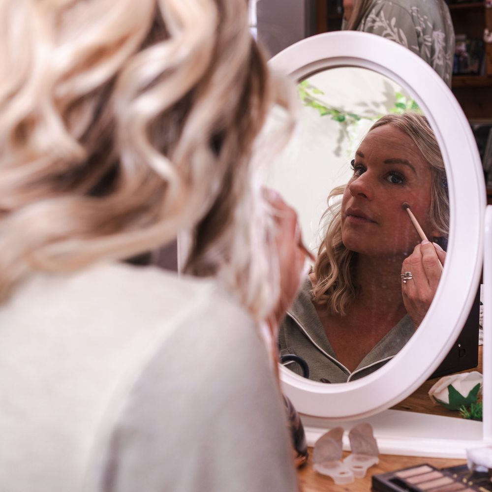 Someone looking in a round vanity mirror while applying makeup in soft lighting.
