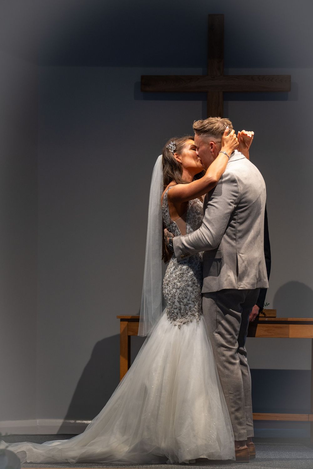 A bride and groom share their first kiss as newlyweds at the altar with a wooden cross in the background.