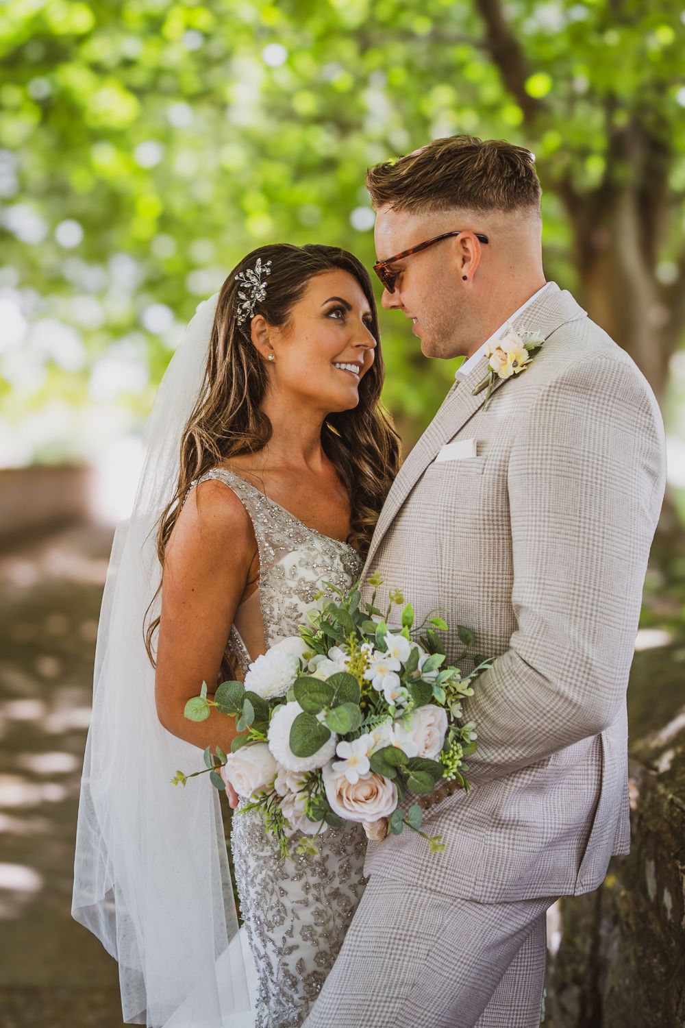 A couple shares romantic moments in their wedding attire against a lush green outdoor backdrop.
