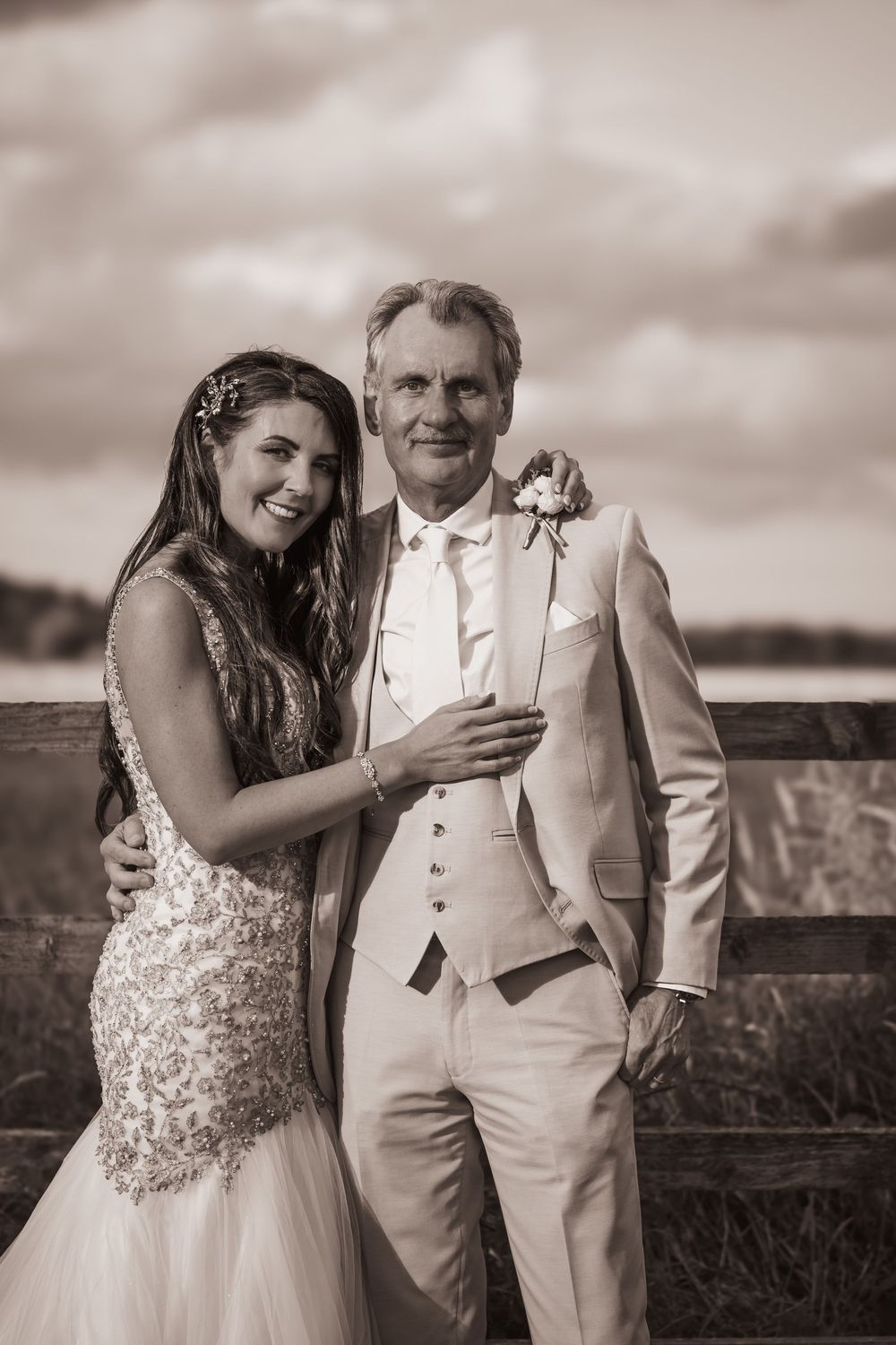 A sepia-toned wedding portrait showing a bride and groom in formal attire posing together outdoors.