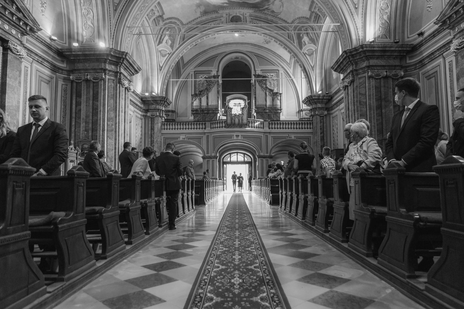 Black and white photograph of a grand church interior with ornate architectural details and long aisle with carpeted runner.