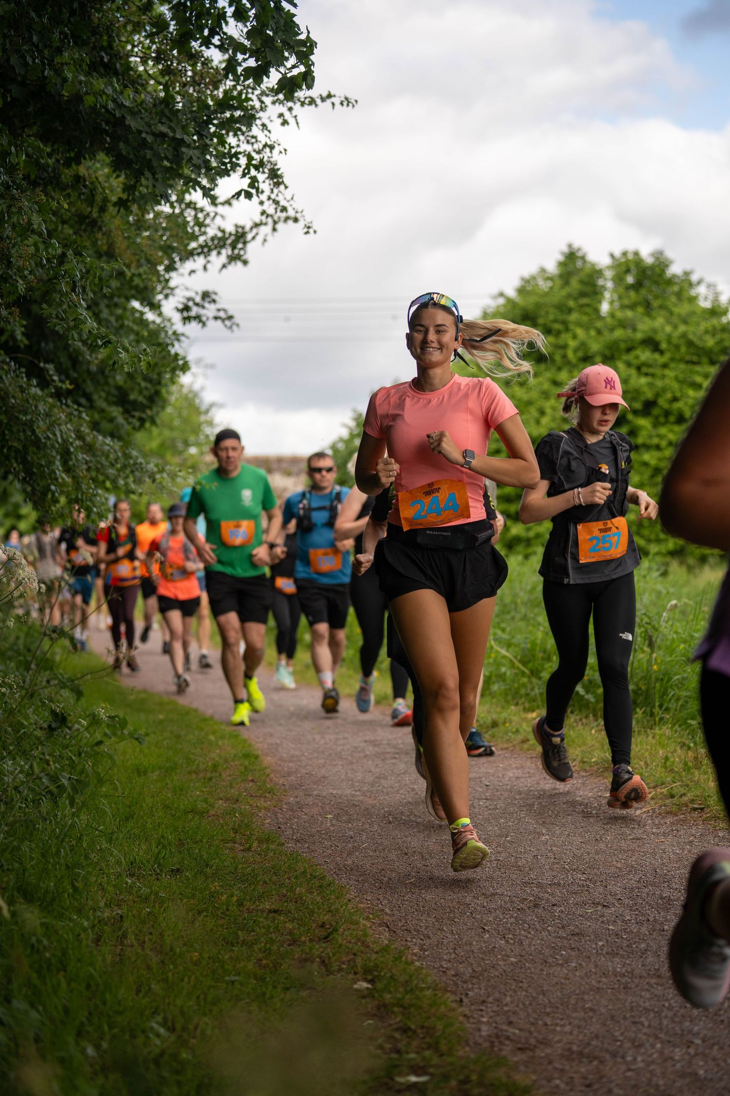 Runners participating in a trail race on a path lined with green trees and vegetation, wearing numbered bibs.