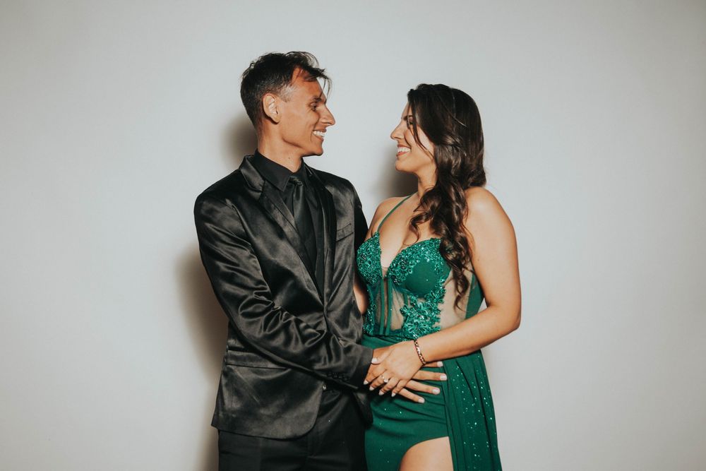 Couple in formal attire dancing and laughing against white studio backdrop.