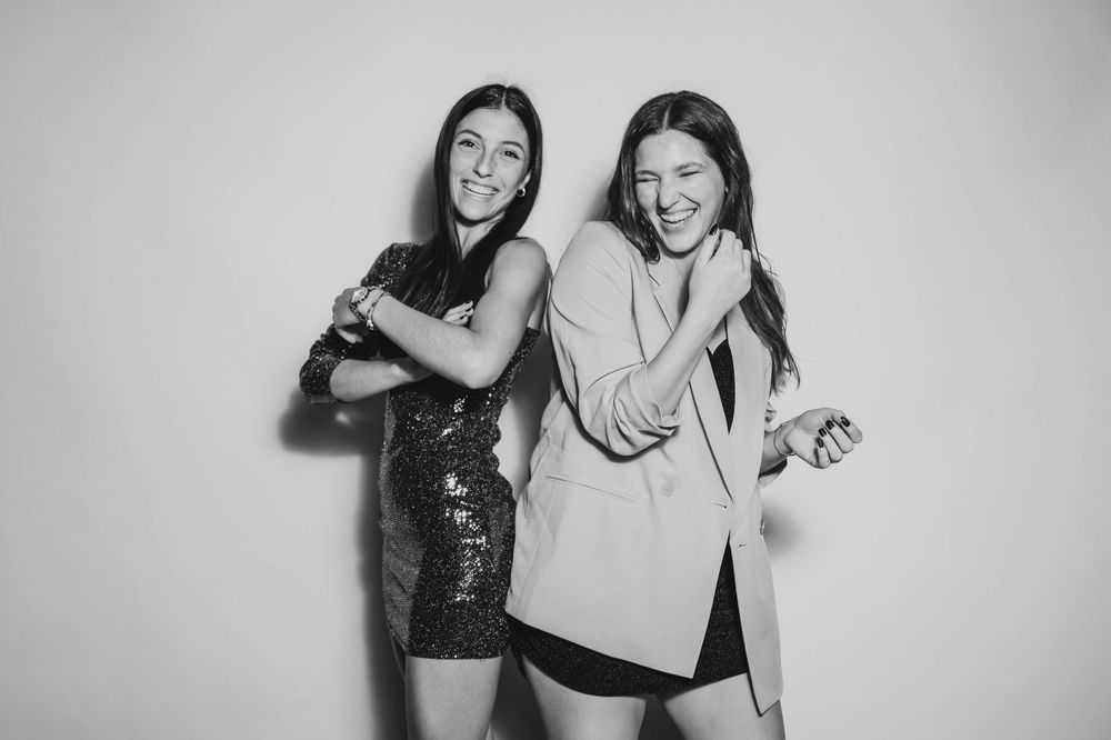 Dos amigas posando y divirtiéndose en el estudio de fotografía móvil sobre un fondo blanco.